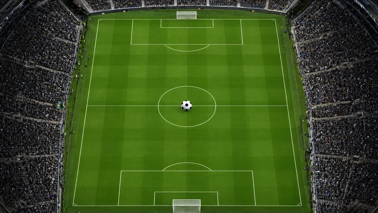 Nachtaufnahme eines beleuchteten Fußballstadions mit Rasen und Mittelkreis aus der Vogelperspektive