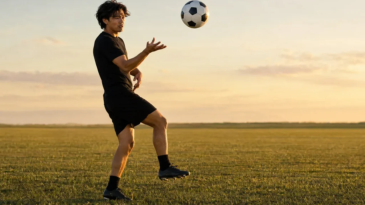 Fußballspieler beim Jonglieren mit rundem Ball auf leerem Trainingsplatz im Abendlicht